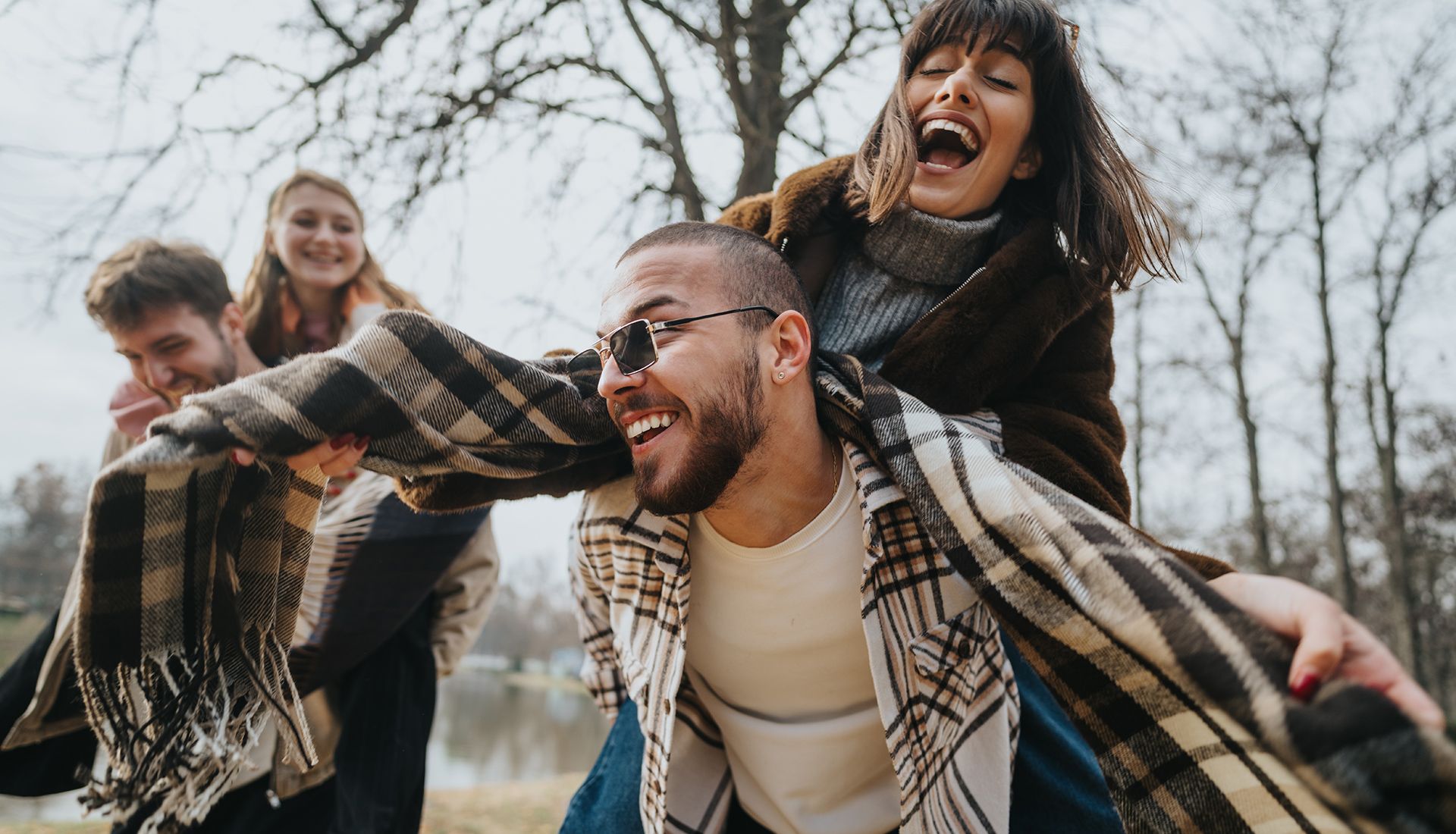 Four friends laughing and playing outside; two people piggybacking.