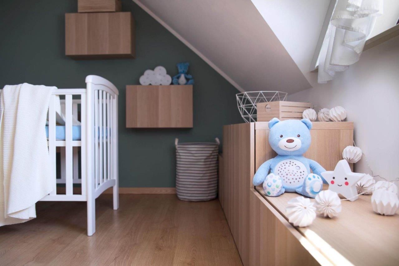 Un orsacchiotto è seduto su uno scaffale in una cameretta dei bambini, accanto a una culla.