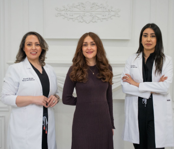 Three medical professionals in white coats standing in a bright clinic hallway