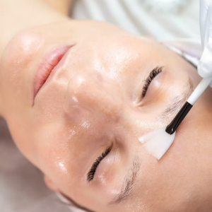 Woman receiving a facial treatment with a white brush applying cream to her forehead.