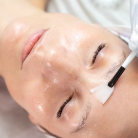 Woman receiving a facial treatment with a white brush applying cream to her forehead.