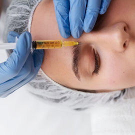 Gloved hands inject yellow liquid into a patient’s eyebrow area with a syringe