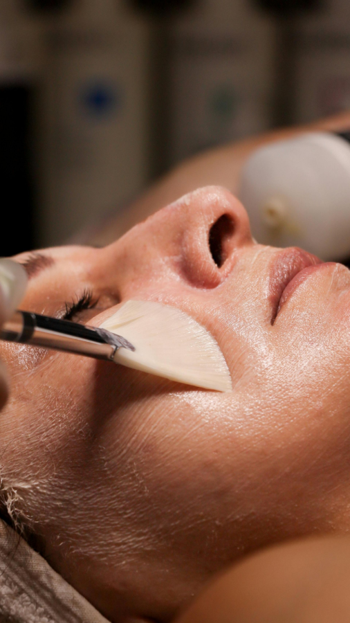Close-up of a facial spa treatment with a brush applying cream to a person's cheek and nose.