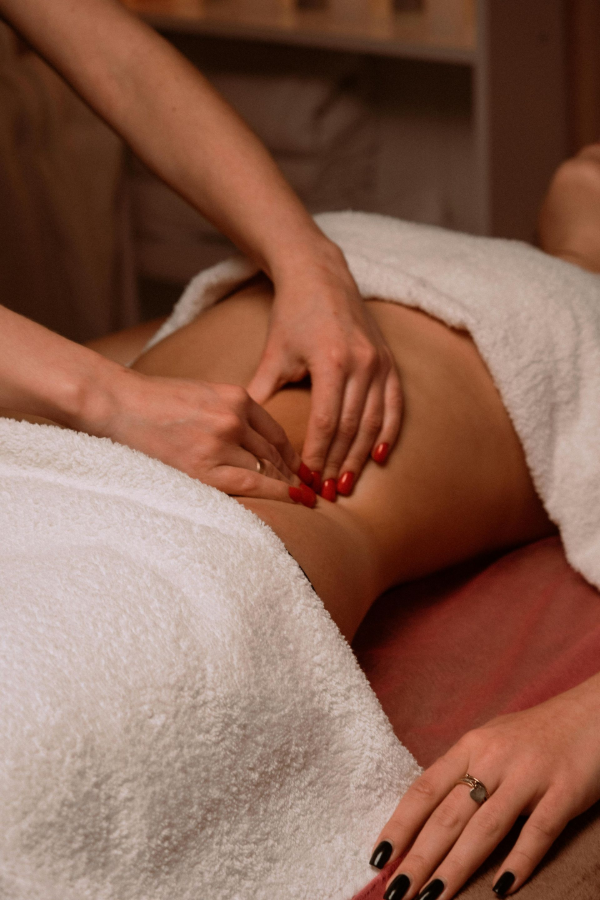 Hands massaging a person’s lower back with white towels in a spa setting