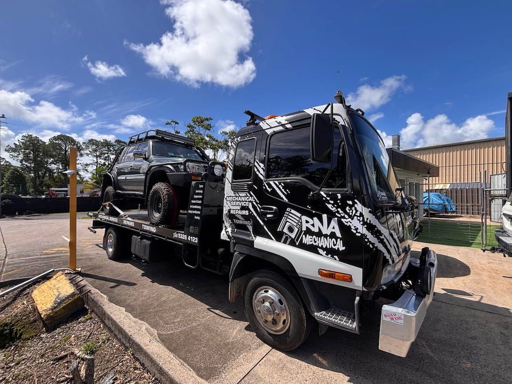 A Tow Truck With a Car on the Back is Parked in a Parking Lot — RNA Mechanical In Nambour, QLD