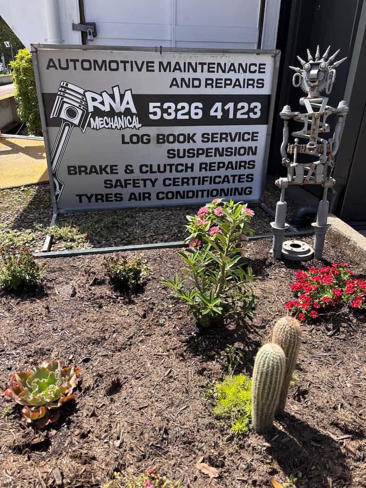 A Sign for Automotive Maintenance and Repairs is Sitting in a Garden — RNA Mechanical In Yandina, QLD