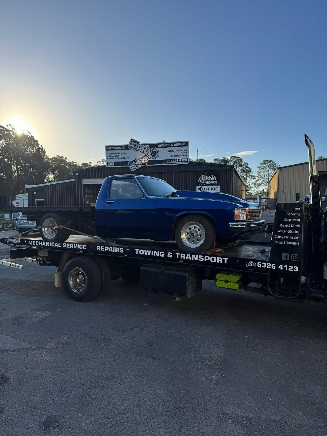 A Blue Car Is Being Towed By A Tow Truck — RNA Mechanical In Yandina, QLD