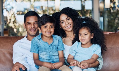 Family of four smiling on a couch indoors: parents, boy, and girl.