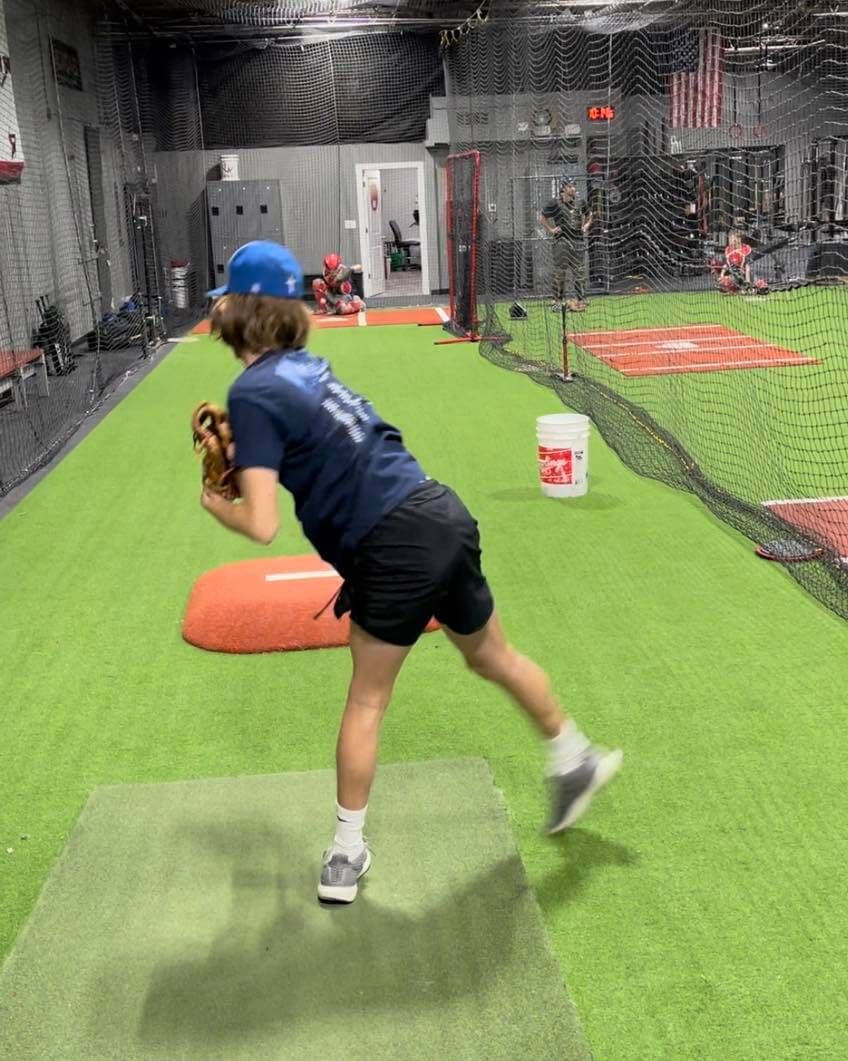 A young athlete is throwing a baseball in a cage.