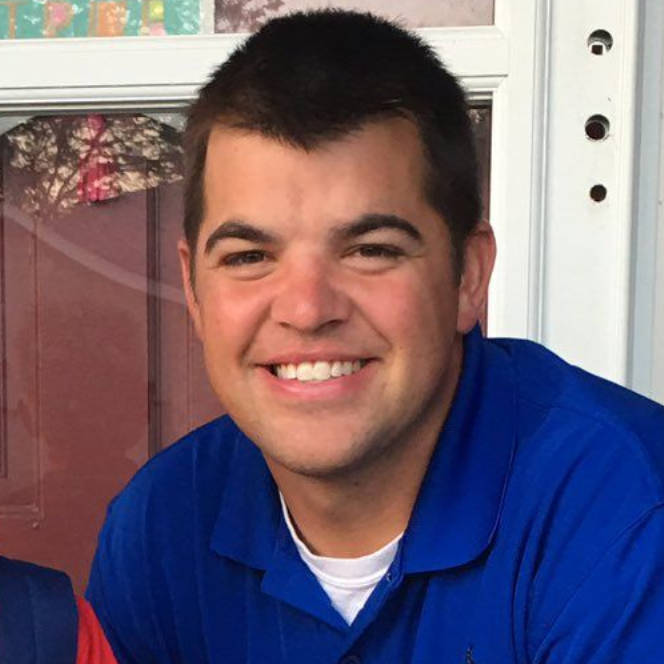 Man smiling, wearing a blue polo shirt, and a white undershirt. Natural light setting.