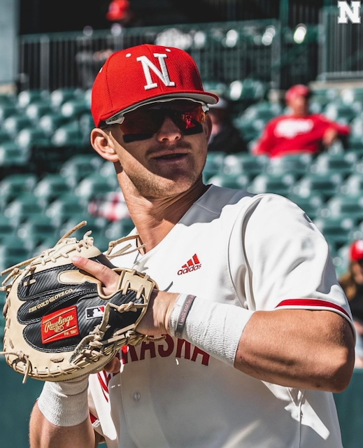Baseball player in red hat and sunglasses, holding a glove, on a field.