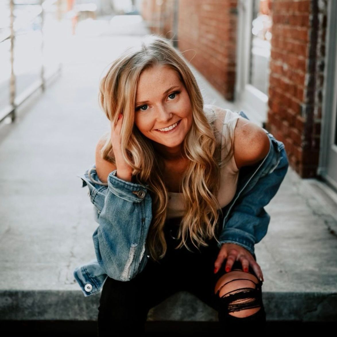 A woman wearing a denim jacket and ripped jeans is smiling