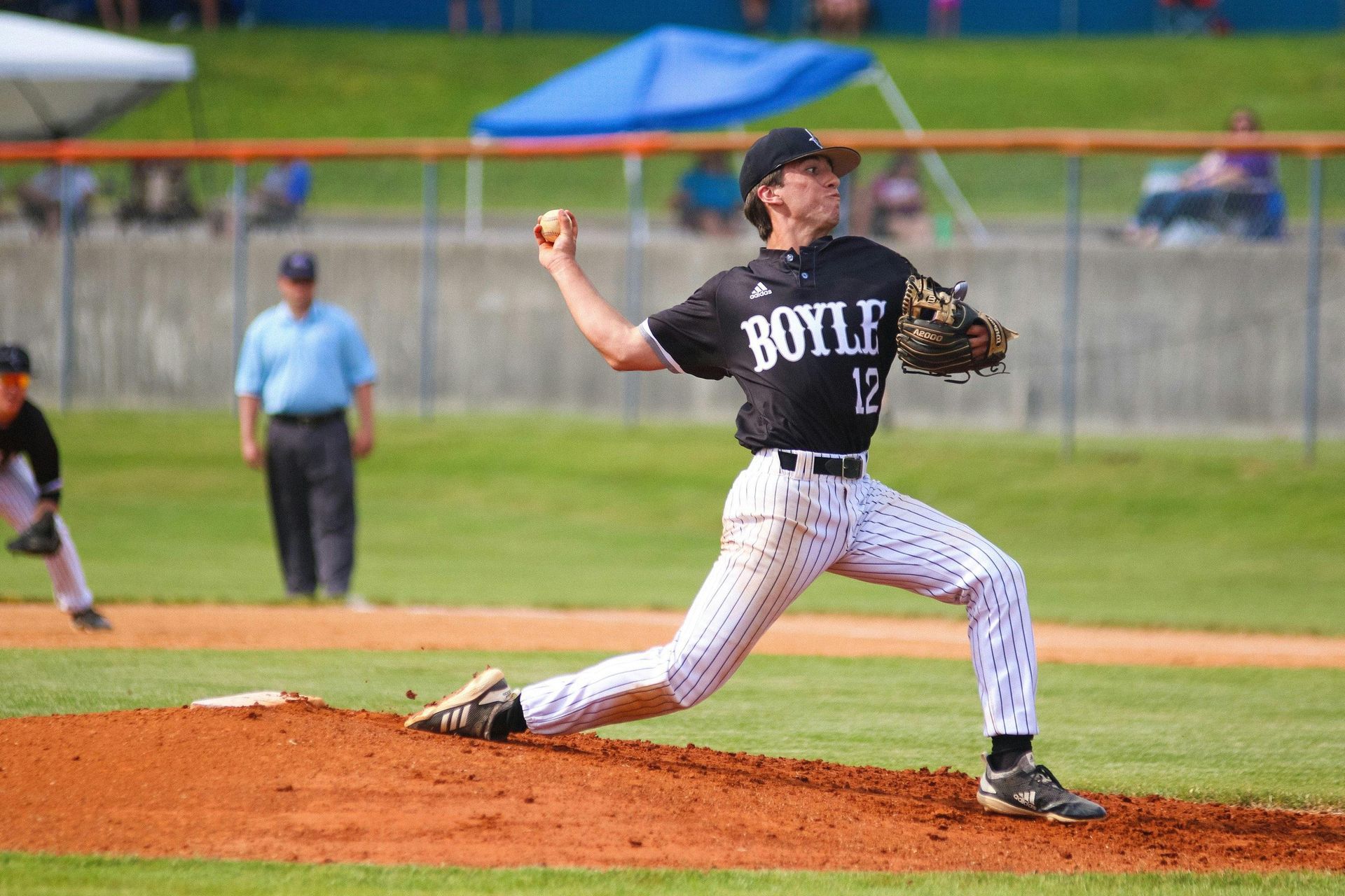 A baseball player with the number 12 on his jersey is pitching the ball.