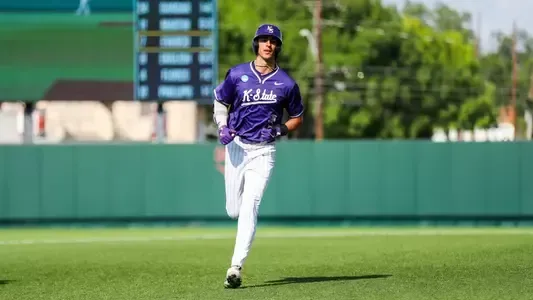 Baseball player in purple jersey running on green field.