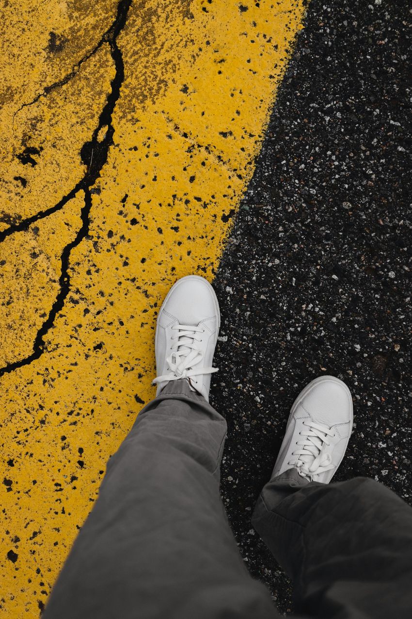 White sneakers on a dark road beside a cracked yellow lane marking