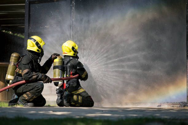 Two firefighters are spraying water on a fire with a hose.