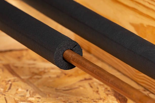 Black foam pipe insulation on copper pipe, against a wood background.
