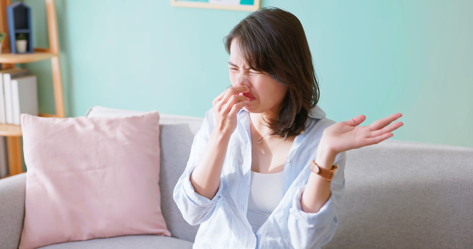 A woman is sitting on a couch covering her nose.