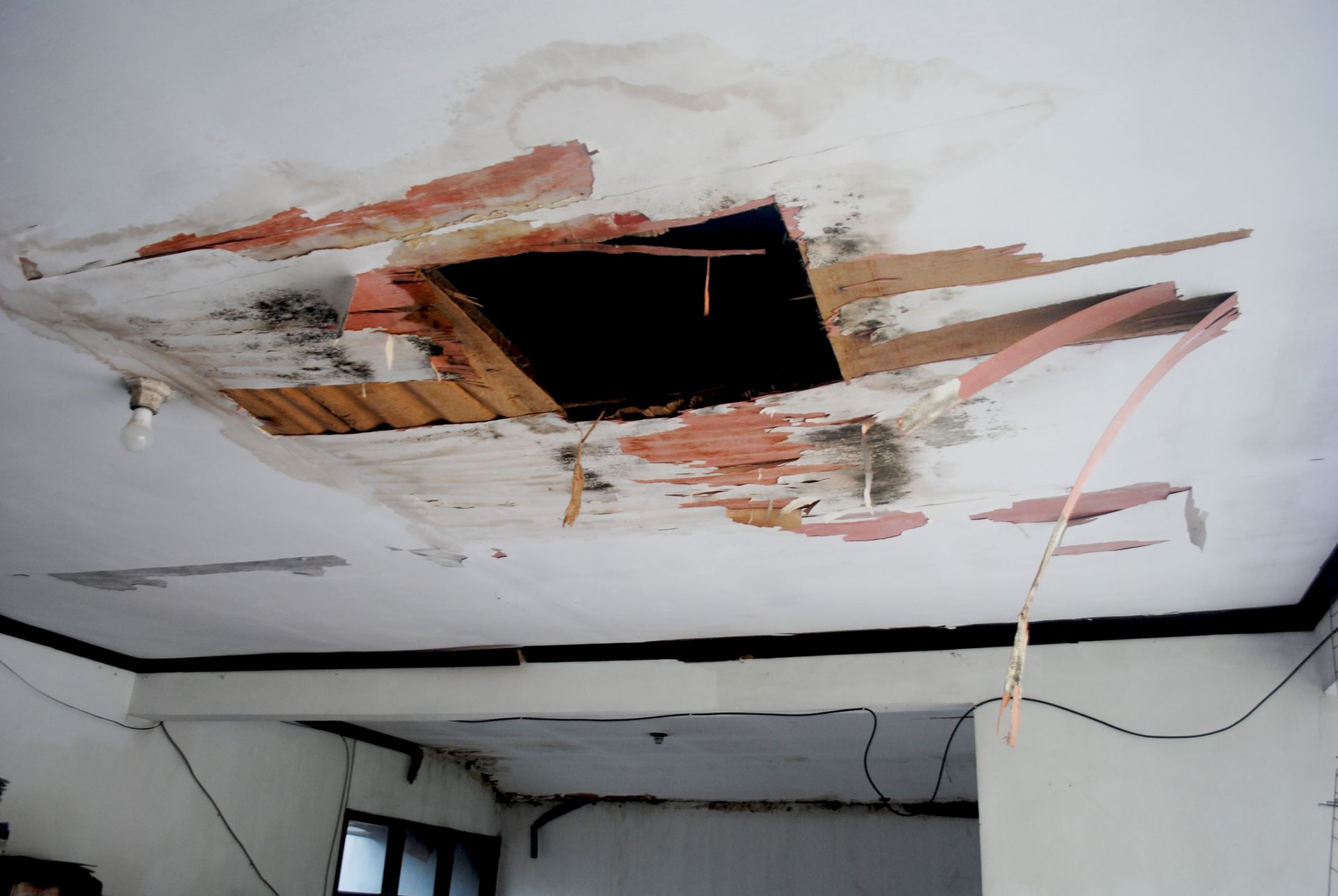 Damaged ceiling with a large hole and water stains; pink paint, exposed wood.