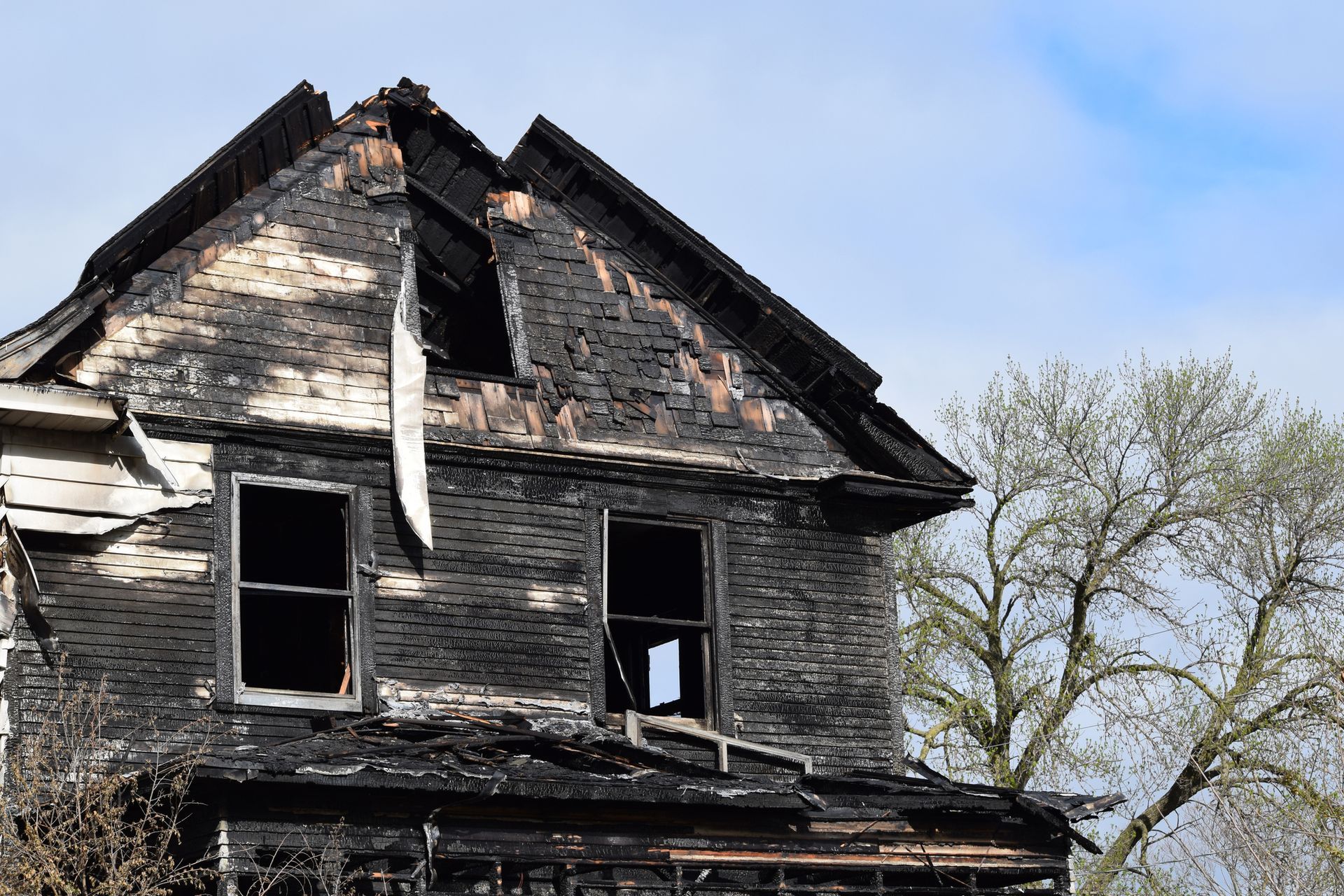 An old abandoned house with a broken roof and a tree in the background.