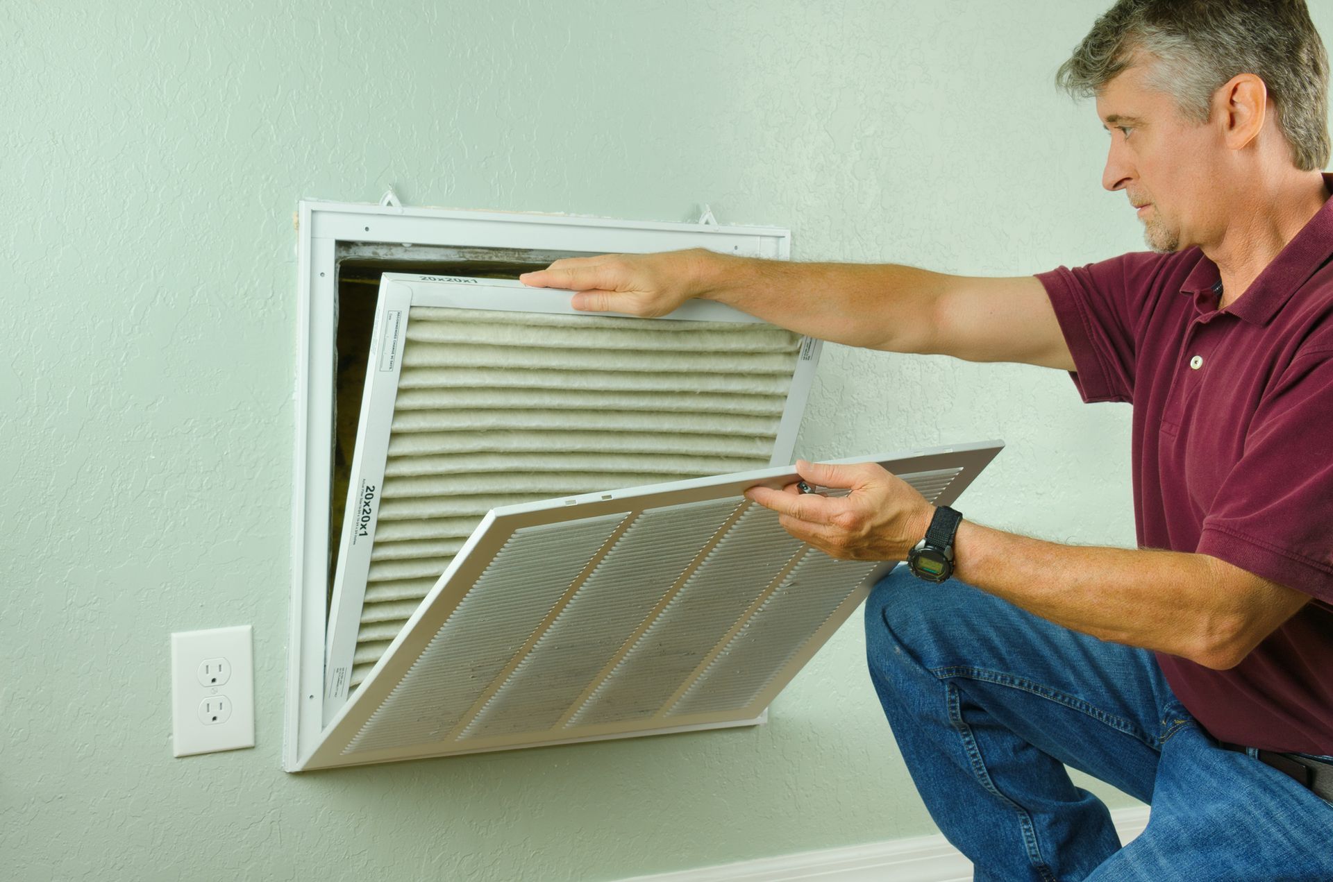 A man is kneeling down to remove a filter from an air vent.