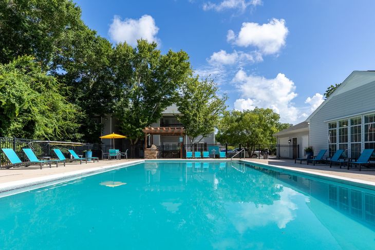 Pool area with turquoise water, blue lounge chairs, and a sunny sky.