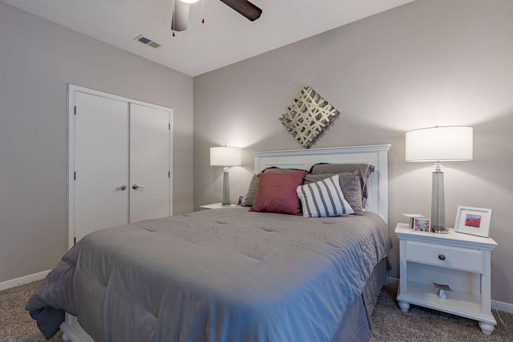 Bedroom with bed, bedside tables, lamps, and closet. Gray and white color scheme, neutral tones.