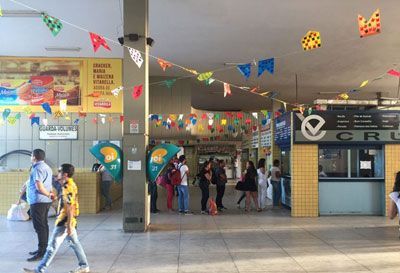 Pessoas em uma estação de ônibus, decorada com bandeiras coloridas.