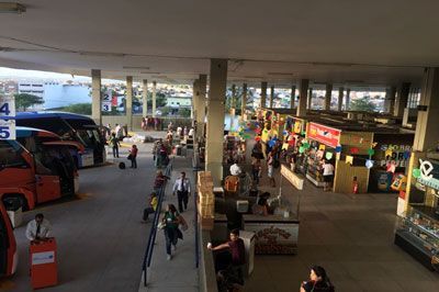Estação rodoviária com pessoas, ônibus, lojas e vista para a água.