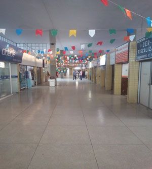 Interior de um prédio bem iluminado com piso de azulejos e lojas em ambos os lados. Bandeirinhas coloridas enfeitam o teto.