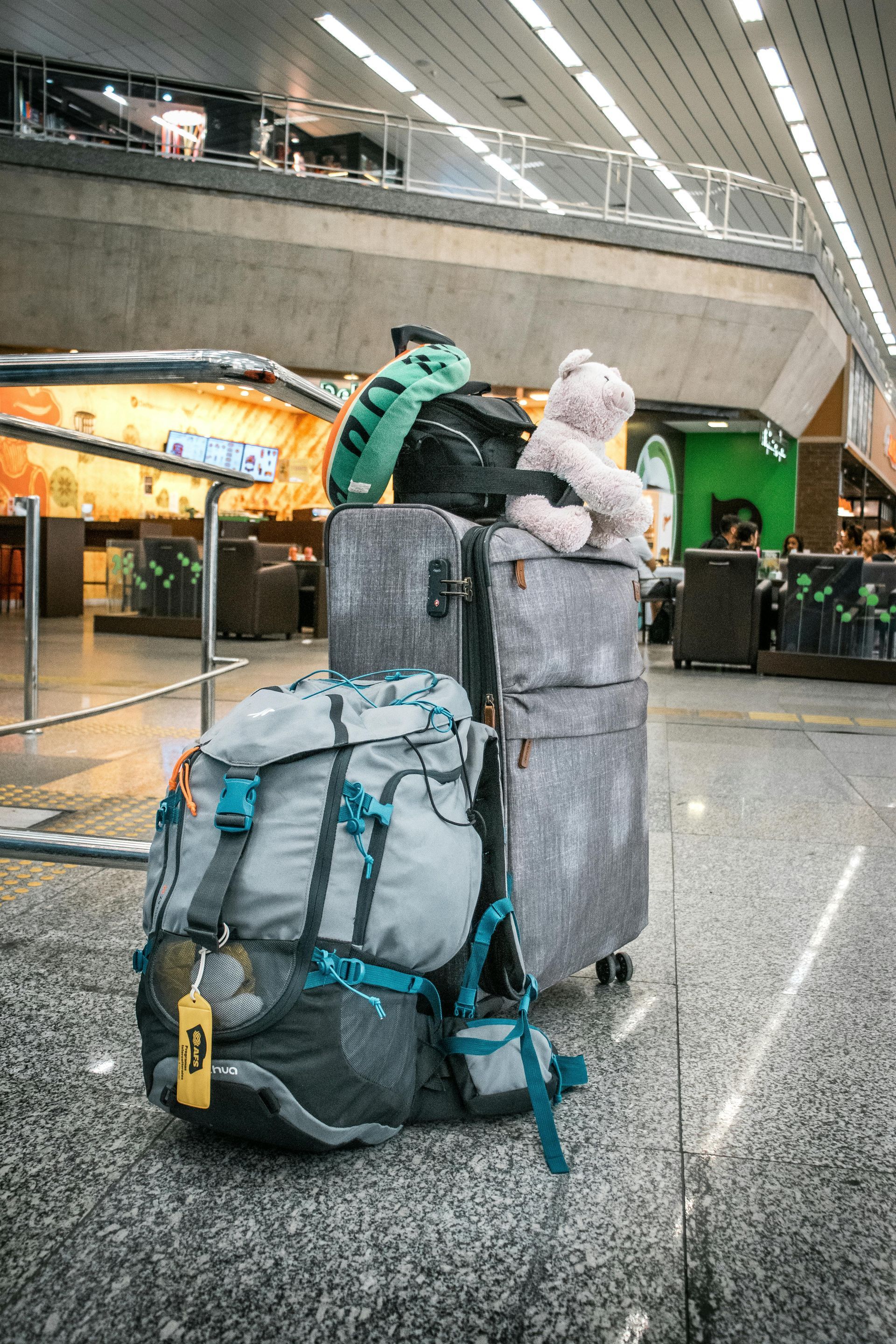 Bagagem empilhada no aeroporto, incluindo uma mochila grande, malas e bichos de pelúcia.