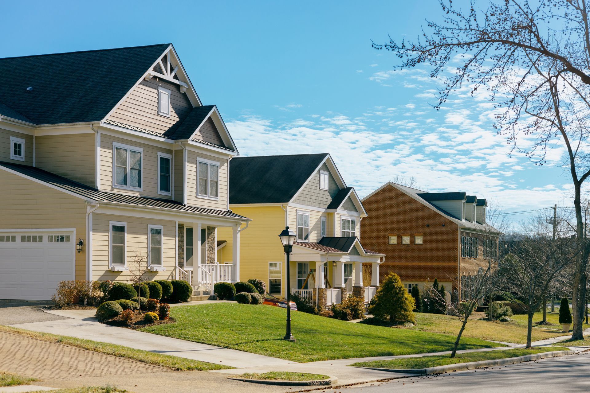 Suburban row of beige and yellow houses with manicured lawns under a clear blue sky