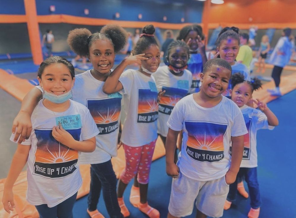 Group of children smiling at trampoline park, wearing matching white t-shirts.