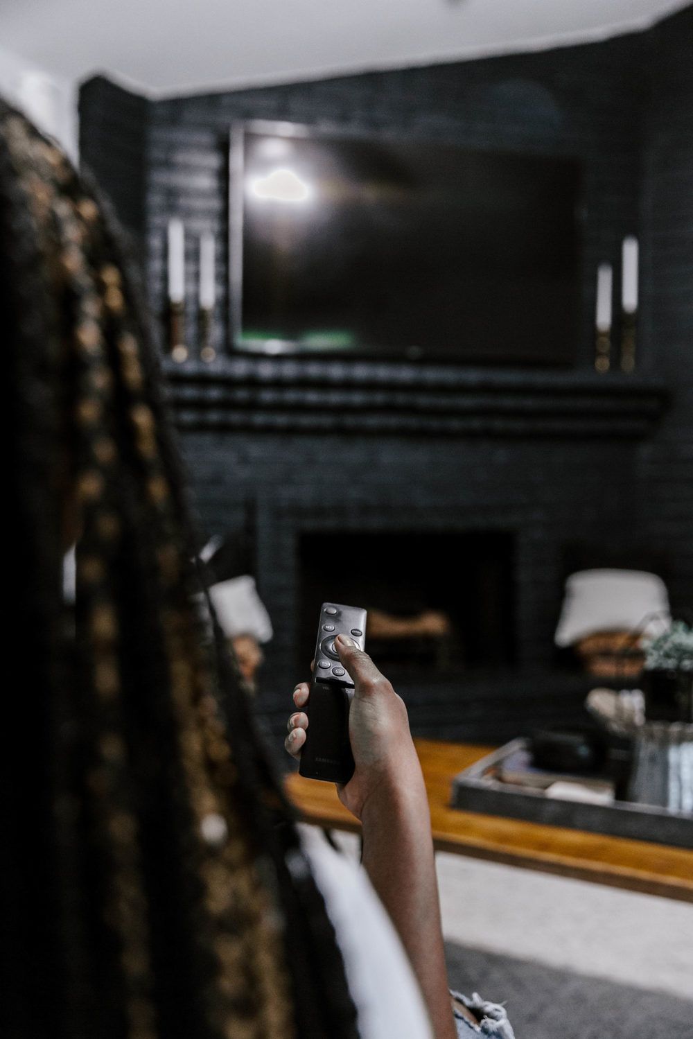 Person holding a remote control, aiming it at a television above a black brick fireplace.