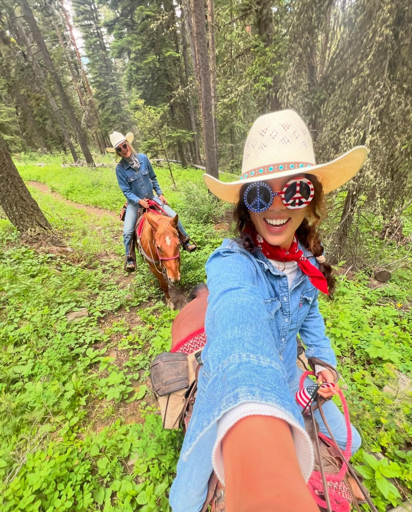 Two women are riding horses in the woods.