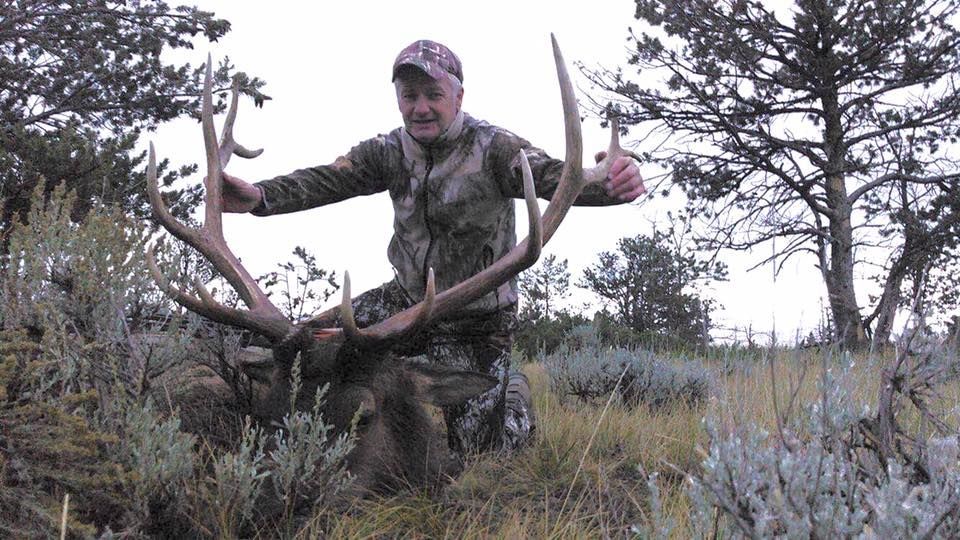 A man is holding a large deer in a field.