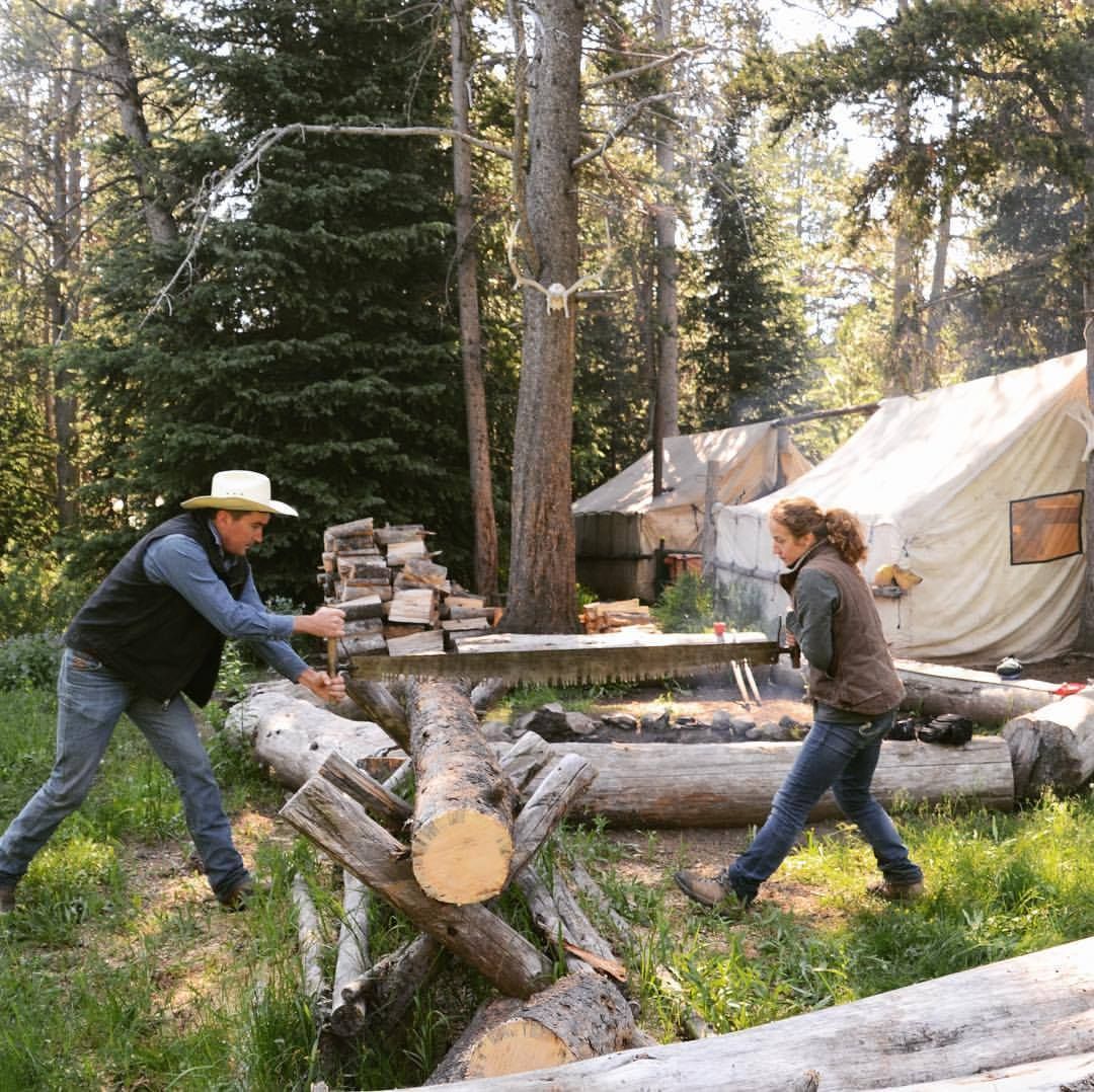 A man and a woman are cutting logs with a saw