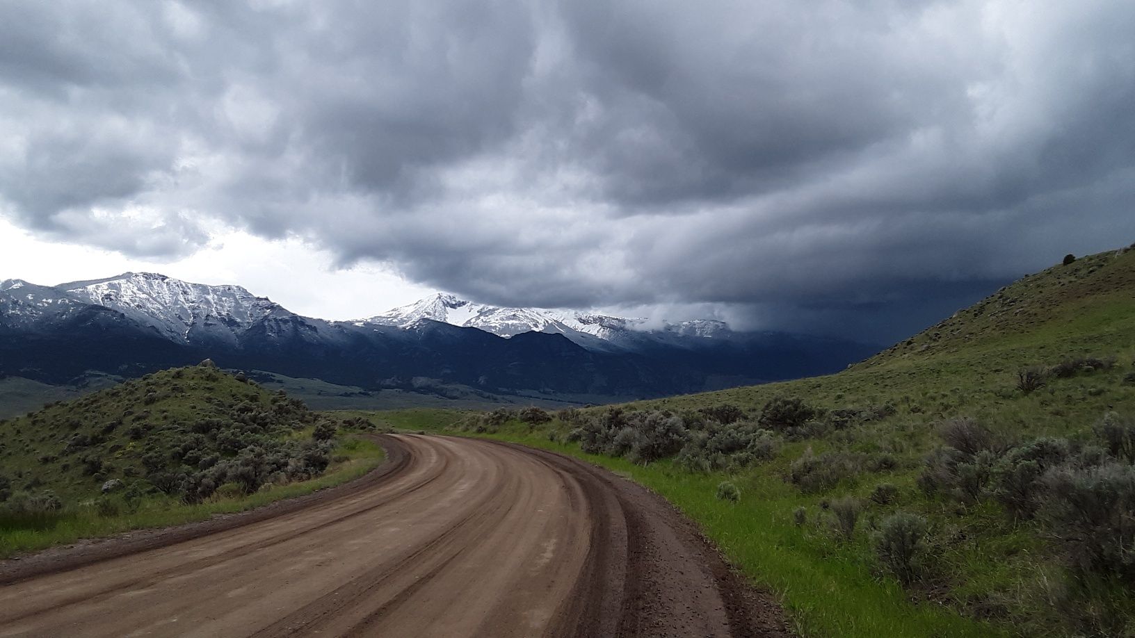 A dirt road with mountains in the background on a cloudy day.
