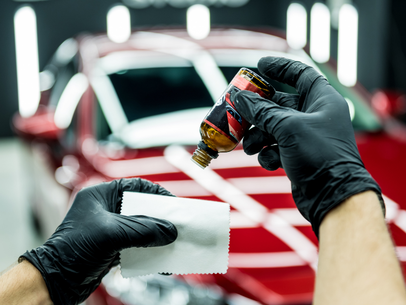 Gloved hands applying polish to a red car in a detailing shop Gloved hands applying car polish to a red vehicle with a cloth in a detailing shop