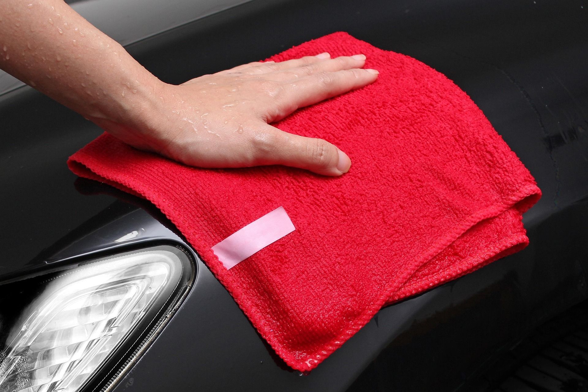 Gloved hands cleaning a car dashboard with a cloth and spray bottle Person polishing a red car hood with a power buffer in a garage