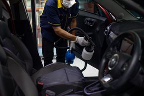 Worker sanitizing the interior of a car with a spray bottle and cloth