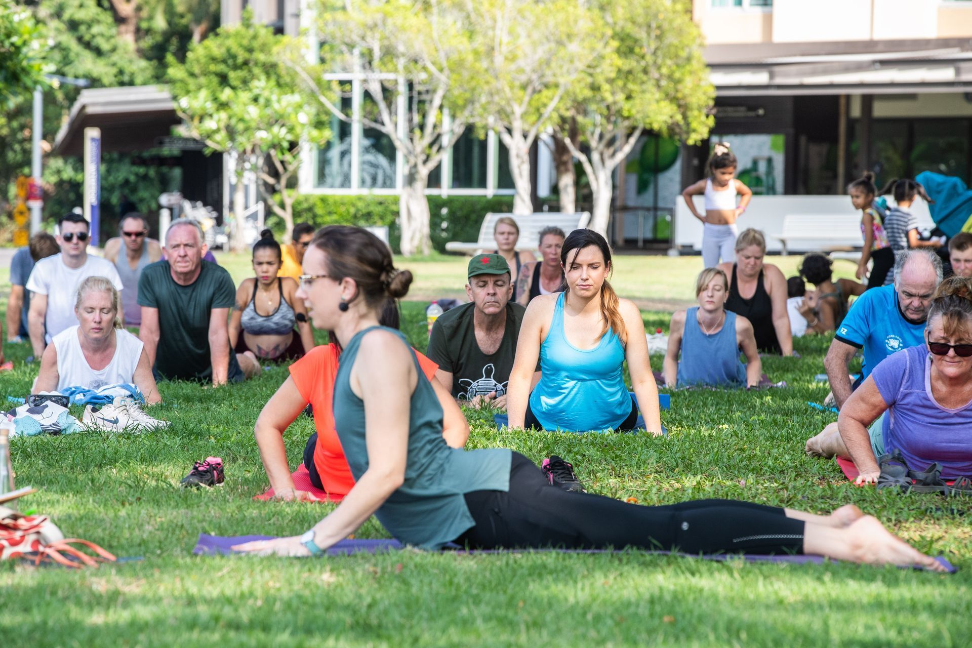People in a park doing yoga outdoors on grass with a woman instructor.