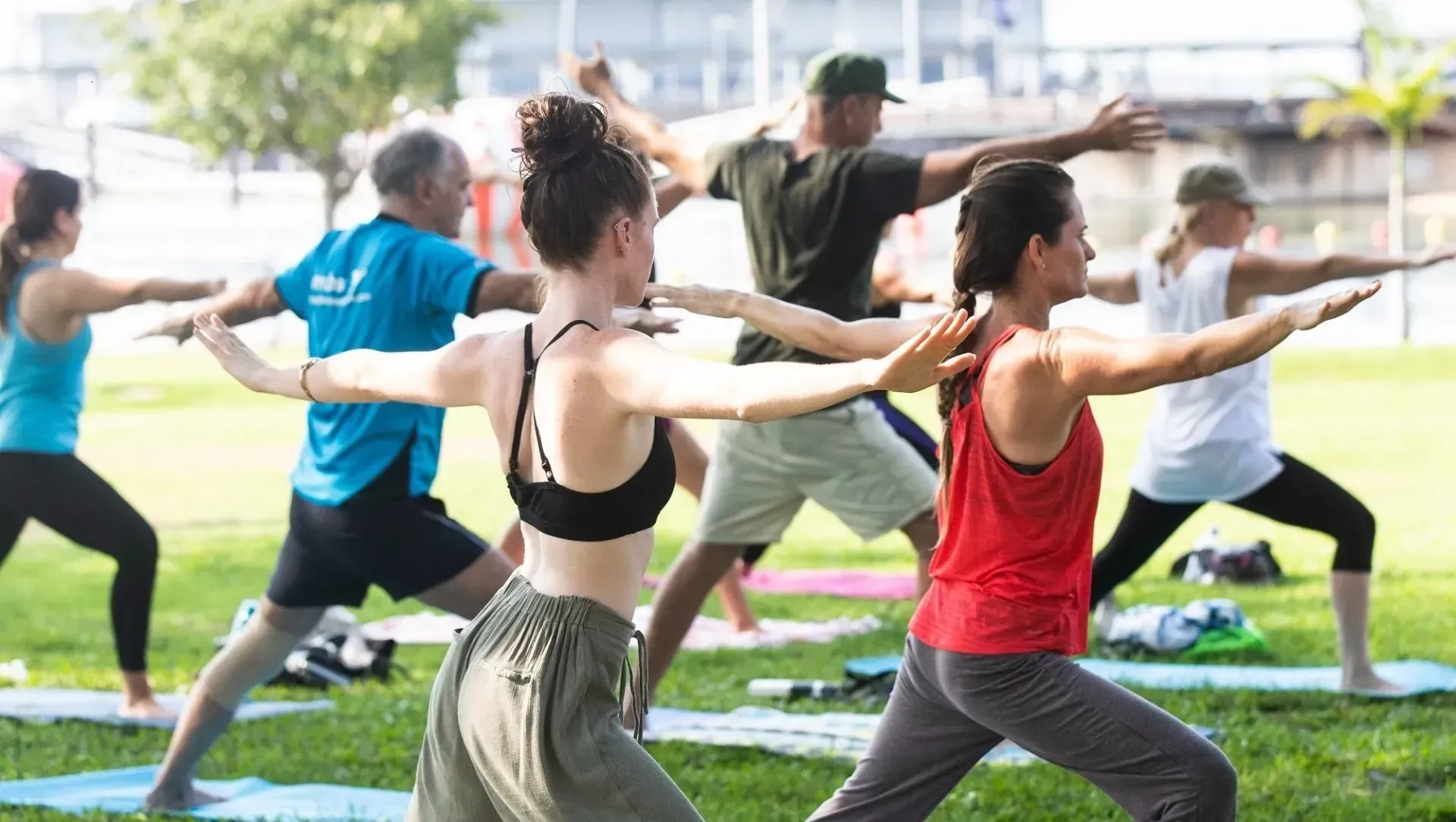People practicing yoga in a park, arms extended. Green grass, blue sky.