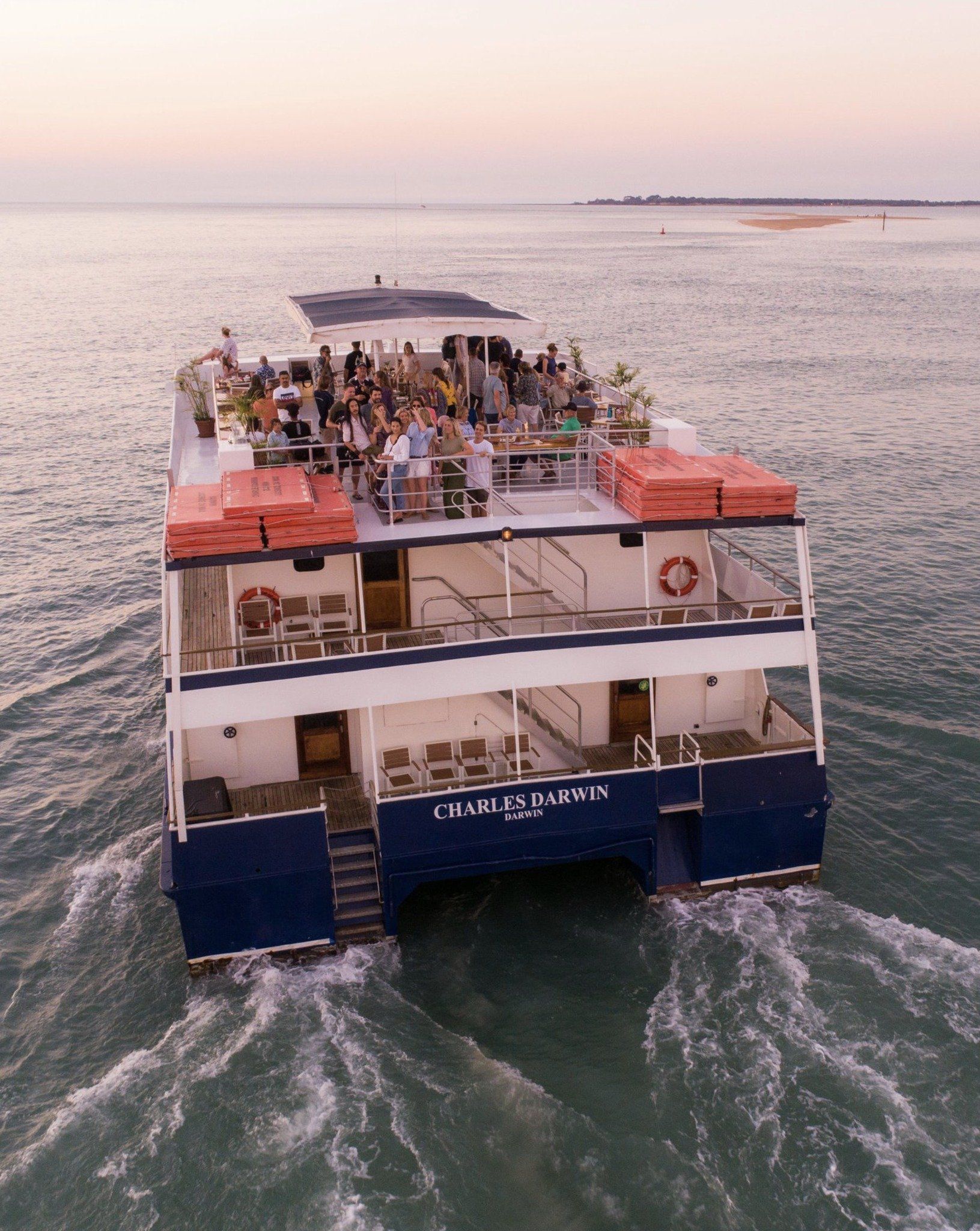 Large blue catamaran with people on top deck sailing on water.