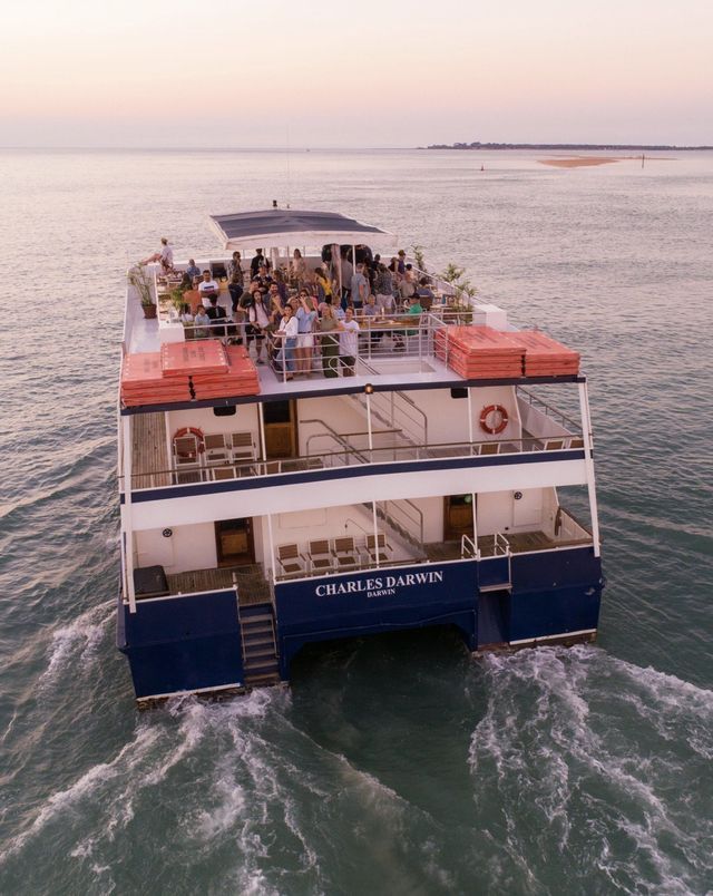 Catamaran cruise ship on the water; people on deck, sunset setting in the background.