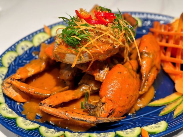 Crab dish with orange sauce on a blue plate, garnished with vegetables.