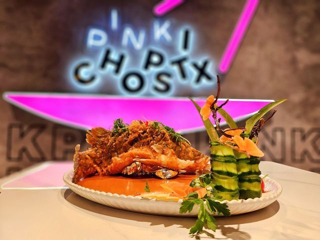 Crispy fish dish with cucumber rolls and sauce, in front of a pink lit restaurant sign.