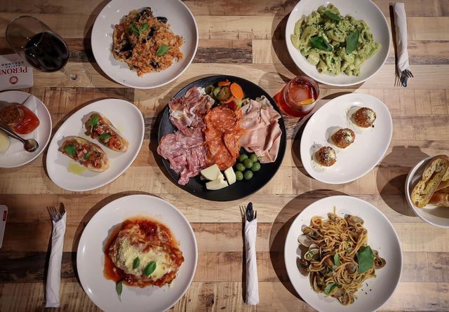 Table of Italian dishes: pasta, meats, appetizers, and wine on a wooden surface.