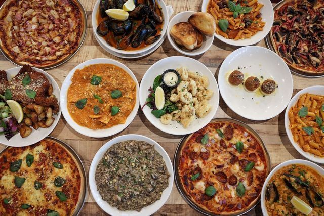 Overhead view of a spread of Italian food, including pizzas, pasta, mussels, and appetizers on a wooden table.