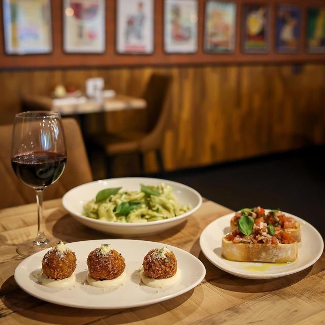 Italian dishes: pasta, bruschetta, and arancini, served with red wine in a restaurant setting.